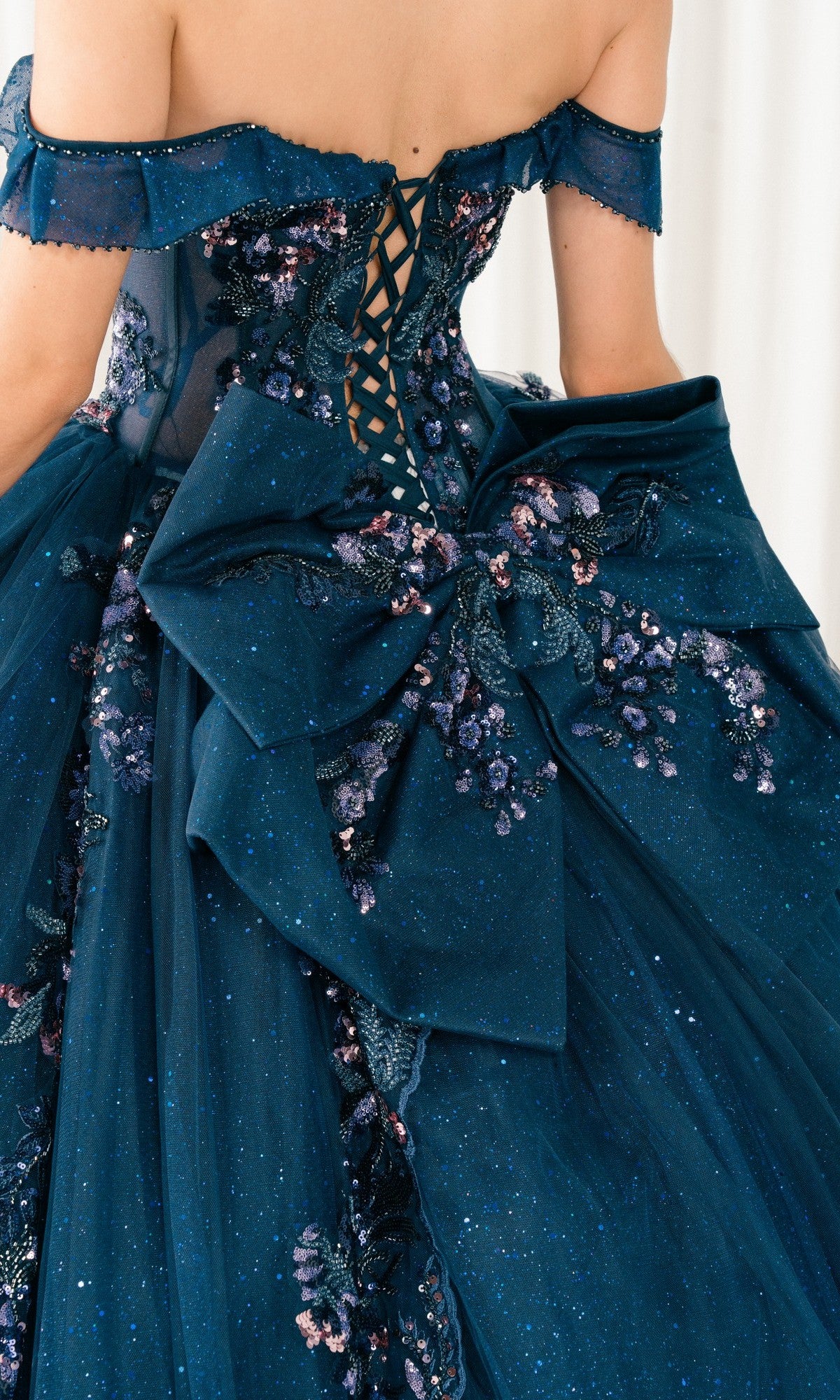 A close-up of the back of the Quinceanera Dress 8440JQ By Cinderella Couture, featuring lace-up detailing, a large decorative bow, and glitter-accented floral embroidery.